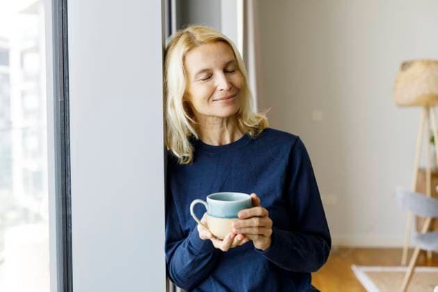 Smiling woman with eyes closed holding tea cup by window at home model released, Symbolfoto property released, TYF00838