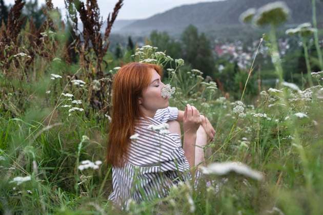 Creative Highlights Symbolbilder Redhead woman smelling wild flower sitting in meadow model released, Symbolfoto, VBUF00579
