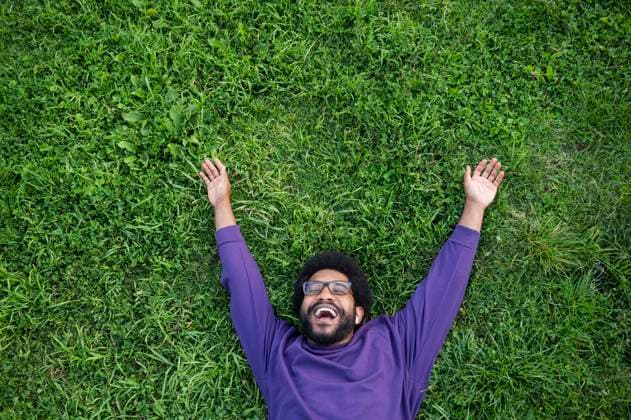 Creative Highlights Symbolbilder Smiling man with arms outstretched lying on green grass in lawn model released, Symbolfoto, VRAF00507