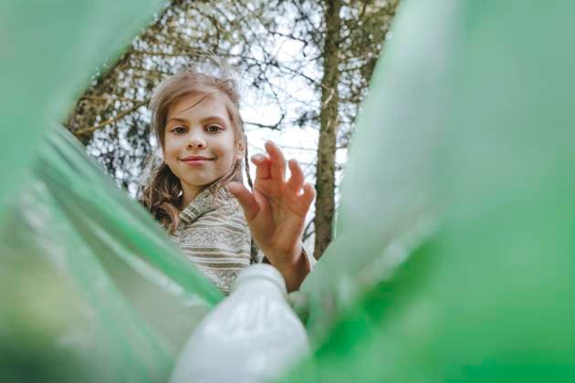 Creative Highlights Symbolbilder Smiling girl putting plastic bottle in garbage bag at forest model released, Symbolfoto, YTF02374