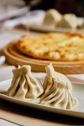 IMAGO Creative, Food, Dumplings A delicious selection of Georgian cuisine, featuring khinkali dumplings on a ceramic plate and khachapuri cheese bread on a wooden serving board in the background Model Released EduardoGarcia_ID21588_633838_002 Copyright: xEduardoxGarciax