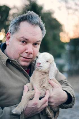 Man holding a newborn goat kid close, both looking at the camera United States, Florida, Floral City R_YWQX24052280-1443785-01 ,model released, Symbolfoto