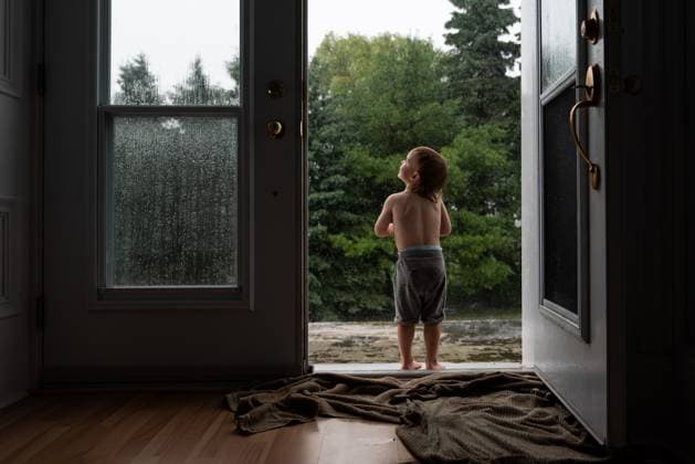 Child stands in doorway looking out at rainy scene with wet trees. Wingham, Ontario, Canada CR_ATBL240528-1433674-01 ,model released, Symbolfoto