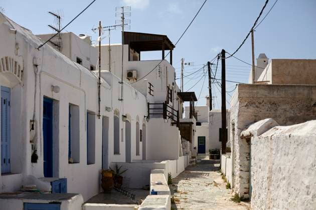 A narrow alley in a traditional Mediterranean village with white buildings and blue doors under a clear sky, with electrical wires crisscrossing overhead. Folegandros Greece bola01001 Copyright: xConnectxImagesx