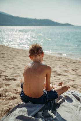 Creative Highlights Symbolbilder Boy sitting on Calcatoggio beach in Corsica, gazing at the sea Piana, Corsica, France R_FFVO240609C-1450264-01 ,model released, Symbolfoto