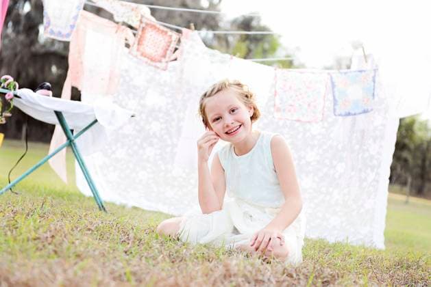 Creative Highlights Symbolbilder Smiling girl sitting on grass near hanging clothes. United States, Florida, Floral City R_YWQX240605C-1449390-01 ,model released, Symbolfoto