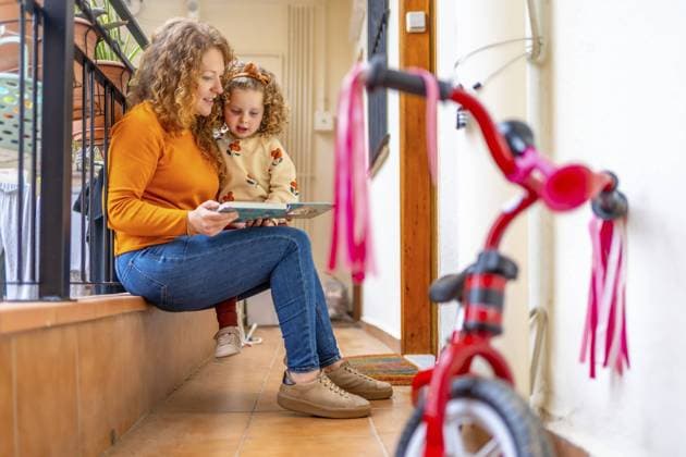 IMAGO Creative, Architektur, Zukunftsmodell Tiny flats Mother reading a book to a girl at the terrace of a apartment