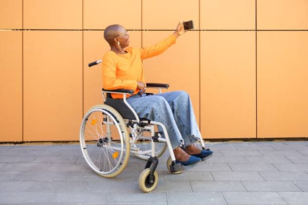 Creative Highlights Symbolbilder An African American businesswoman in a wheelchair captures a selfie against a modern orange backdrop, showcasing independence and technology embrace Model Released DavidMunoz_ID22272_651067_055 Copyright: xDavidxMunozx