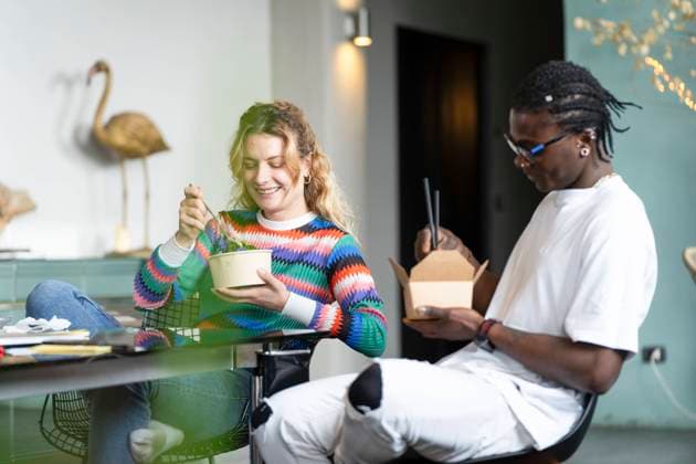 A happy young multiethnic couple takes a break from smart working at home, enjoying a meal together in a cozy, modern interior with nature illustrations Model Released VictorCuenca_ID22085_646426_029 Copyright: xVictorxCuencax RECORD DATE NOT STATED