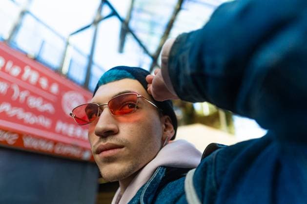 Creative Highlights Symbolbilder A modern, trendy young man sports vibrant blue hair and red tinted sunglasses Set against a lively urban backdrop with signage, he effortlessly radiates a hip and youthful vibe Model Released VictorCuenca_ID22089_646501_026 Copyright: xVictorxCuencax