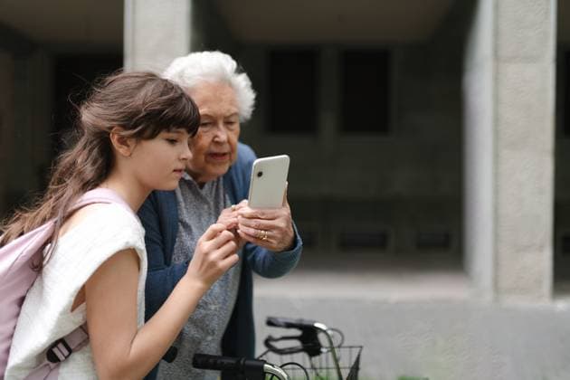 Creative Highlights Symbolbilder Grandma picking up young girl from school at afternoon. Granddaughter showing something on smartphone to senior grandmother, teaching her how to work with technology. Grandma picking up young girl from school at afternoon. Granddaughter showing something on smartphone to senior grandmother, teaching her how to work with modern technology. model released