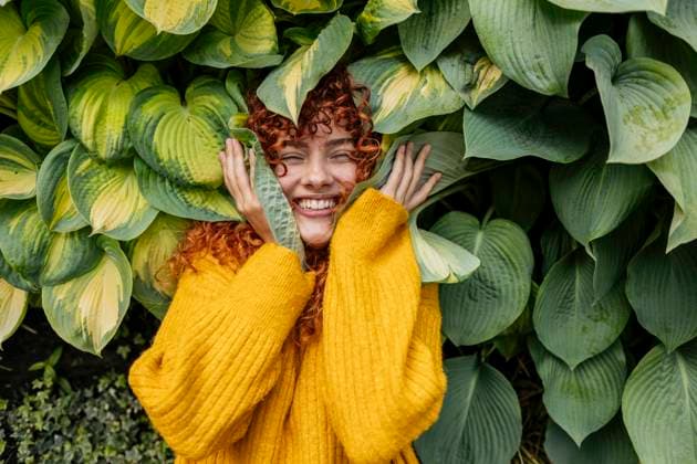 Creative Highlights Symbolbilder Cheerful redhead young woman with curly hair amidst green leaves model released, Symbolfoto, JCCMF11837