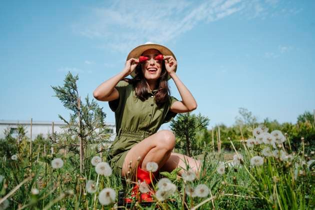 Creative Highlights Symbolbilder Happy playful young farmer holding strawberries in front of eyes crouching near dandelions at garden on sunny day model released, Symbolfoto property released, MDOF02255