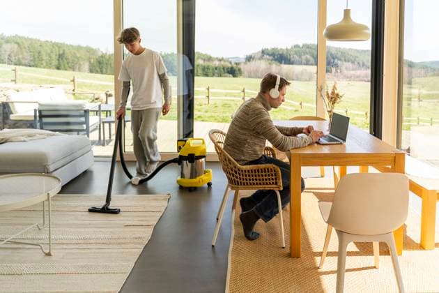 IMAGO Creative, Frühling, Frühjahrsputz Father working on laptop at table by teenage son vacuuming house model released, Symbolfoto property released, NJAF01113