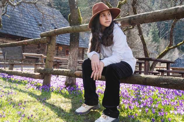 IMAGO Creative, Frühling, Licht und Sonne Girl wearing hat and sitting on wooden fence near flowers at farm model released, Symbolfoto, OSF02554