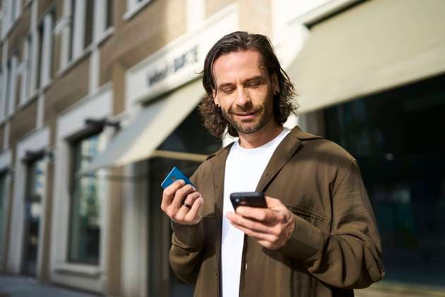 Smiling mature man using smart phone doing online shopping through credit card on sunny day model released, Symbolfoto, PNEF02939