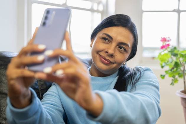 Woman sitting on sofa and using smartphone to take selfie model released Copyright: xCulturaxCreativex