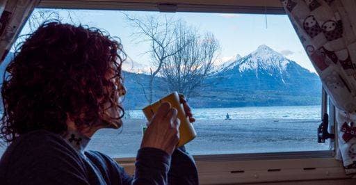 A woman enjoying a hot beverage in a camper van with a scenic view of a snow-capped mountain and lake, Interlaken, Switzerland. 24904950 ,model released, Symbolfoto RECORD DATE NOT STATED
