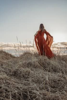 Creative Highlights Symbolbilder Woman in red dress stands in wild Icelandic grass at sunset Hvolsvöllur, Rangárþing eystra, Iceland CR_FFVO240619F6-1464348-01 ,model released, Symbolfoto