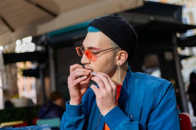 Creative Highlights Symbolbilder A stylish young man enjoys a hamburger at a street cafe He™s dressed in a modern blue jacket and sports teal hair under a black beanie, with orange-tinted glasses Model Released VictorCuenca_ID22089_646529_045 Copyright: xVictorxCuencax