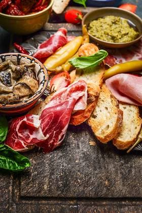 IMAGO Creative, Food, Tapas Italian smoked ham Prosciutto with crostini bread and specialties for antipasti on rustic wooden background, close up ,model released, Symbolfoto
