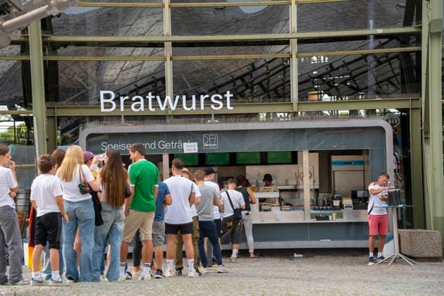 Fanzone München zur UEFA Euro-2024 Europameisterschaft beim Public Viewing. Menschen und Fans stehen Schlange, bzw. Warteschlange um an Bier (Getränke) und Bratwurst (Essen, Lebensmittel) zu kommen.