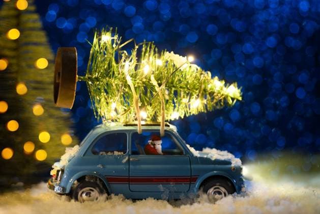 Santa Claus in blue retro toy car delivering Christmas or New Year illuminated tree on festive background. Santa delivering Christmas or New Year tree ,model released, Symbolfoto