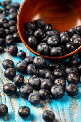 Scattered blueberries from a wooden bowl on a blue background ,model released, Symbolfoto