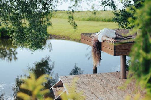 Creative Highlights Symbolbilder A woman relaxing on a wooden deck by a serene pond, surrounded by lush greenery on a sunny day 25067513 ,model released, Symbolfoto RECORD DATE NOT STATED