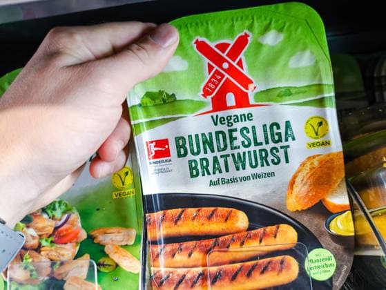 Bavaria, Germany - July 10, 2024: Customer holding a pack of vegan Bundesliga bratwurst from the Rügenwalder Mühle brand. Meat substitute *** Kunde hält eine Packung vegane Bundesliga Bratwurst von der Marke Rügenwalder Mühle in der Hand. Fleischersatzprodukt