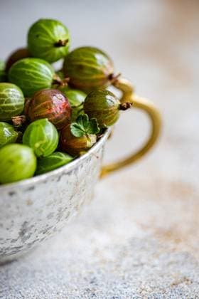 Close-up of fresh organic gooseberries in a rustic, tarnished metal cup set against a soft-focus background. The vibrant green and red tones of the berries highlight their ripeness and natural appeal. Model Released AnnaBogush_ID22657_660675_002 Copyright: xAnnaxBogushx