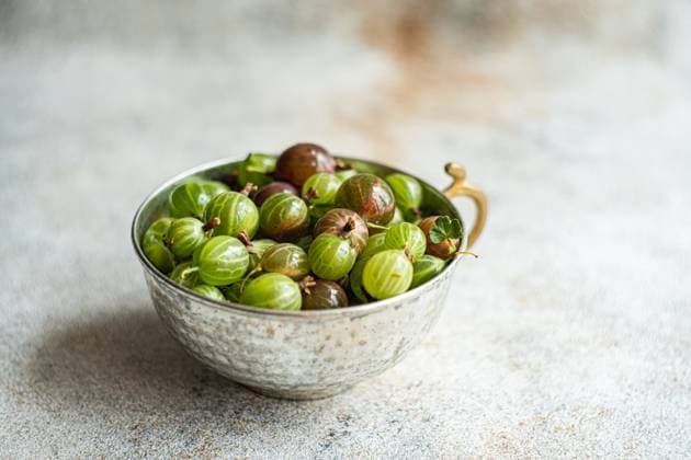 From above, a variety of fresh organic gooseberries in hues of green and burgundy rest in an ornate metal bowl on a textured grey surface, with subtle lighting enhancing their natural sheen. Model Released AnnaBogush_ID22657_660678_004 Copyright: xAnnaxBogushx
