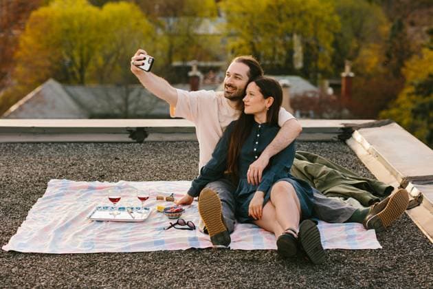 IMAGO Creative, Lifestyle, Frühling in der Stadt A man and woman share a cozy picnic on a rooftop, capturing the moment with a selfie. Surrounded by lush, green trees and urban views, they revel in spring s beauty. Model Released CamilleGirard_ID21717_637062_005 Copyright: xCamillexGirardx