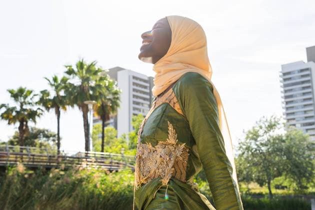 IMAGO Creative, Lifestyle, Frühling in der Stadt A joyful woman in an elegant green dress and hijab basks in the sunny outdoors, smiling brightly The background features urban buildings, lush greenery, and palm trees, creating a vibrant scene Model Released DavidMunoz_ID22571_658455_025 Copyright: xDavidxMunozx