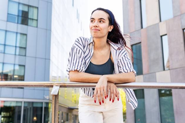 IMAGO Creative, Lifestyle, Frühling in der Stadt A young woman smiles gently as she leans on a railing, surrounded by modern urban architecture Her striped blouse and casual style capture a relaxed spring mood Model Released DavidMunoz_ID22797_663710_007 Copyright: xDavidxMunozx