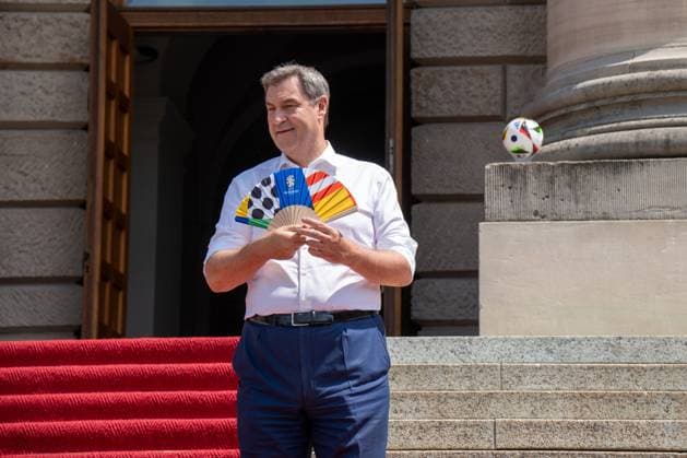 Ministerpräsident von Bayern Dr. Markus Söder bei der Ehrung der Freiwilligen Helfer der EM den Volunteers. Ihm ist heiß und er kühlt sich mit einem UEFA Fächer