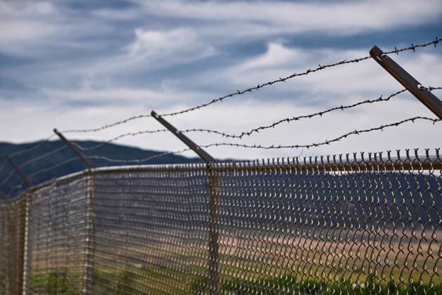 Sicherheitszaun und Stacheldraht vor einer ländlichen Landschaft, symbolisch für Grenzen und Beschränkungen