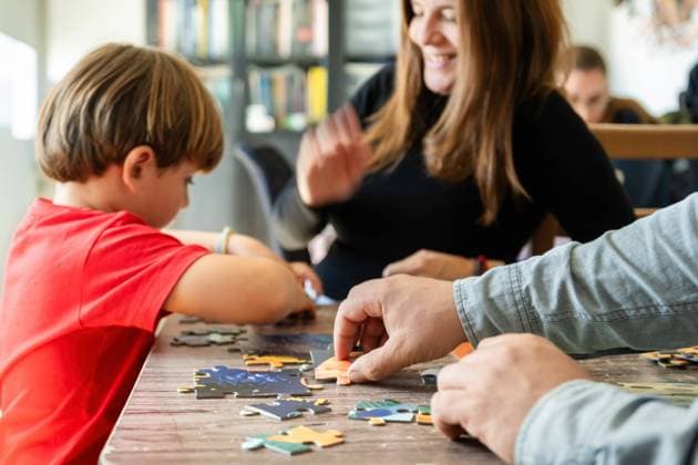 Focused boy assembling jigsaw puzzle with happy crop parents Side view of little boy playing wooden jigsaw puzzle at table with cheerful supportive parents at home Model Released GabrielTrujillo_ID22403_654558_001 Copyright: xx