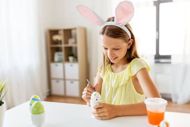 easter, holidays and people concept - happy girl wearing bunny ears headband coloring eggs with colors and brush at home. happy girl coloring easter eggs at home ,model released, Symbolfoto