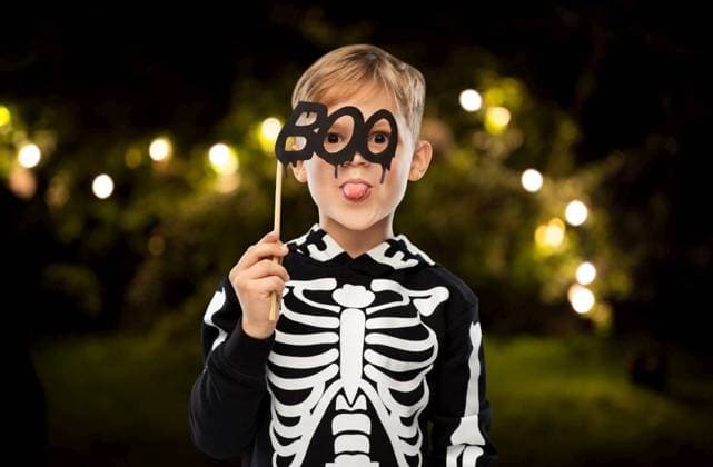 halloween, holiday and childhood concept - smiling boy in black costume of skeleton showing tongue over night park and garland lights on background. boy in halloween costume of skeleton making faces ,model released, Symbolfoto