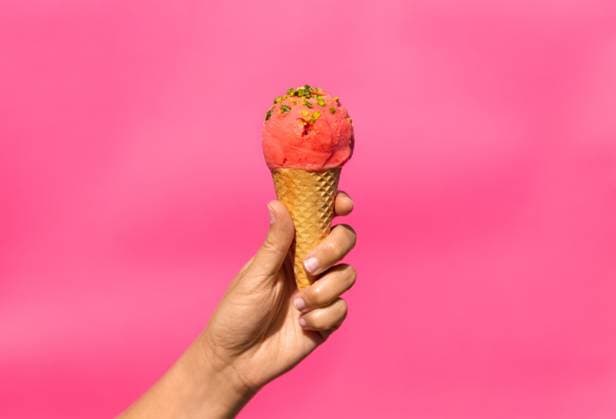 food, dessert and eating concept - close up of hand holding ice cream in waffle cone with pistachio sprinkles over pink background. close up of hand holding waffle ice cream cone ,model released, Symbolfoto