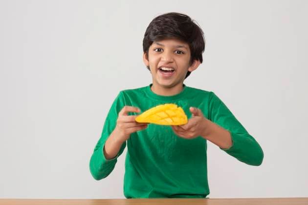 Portrait of happy boy holding a segmented slice of mango ,model released, Symbolfoto