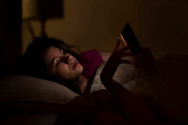 Woman Chatting on smartphone at night while lying on bed ,model released, Symbolfoto