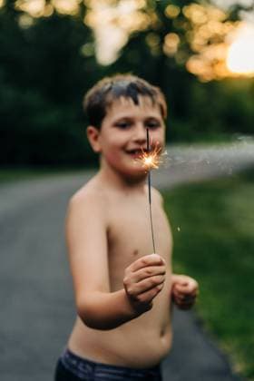 Creative Highlights Symbolfotos Close-up of a boy holding a lit sparkler, smiling at sunset North Andover, Massachusetts, United States R_FKNH240717-1488836-01 ,model released, Symbolfoto