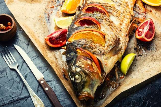 Delicious fish carp grilled whole with lemon and oranges.. Prepared baked carp on baking paper ,model released, Symbolfoto