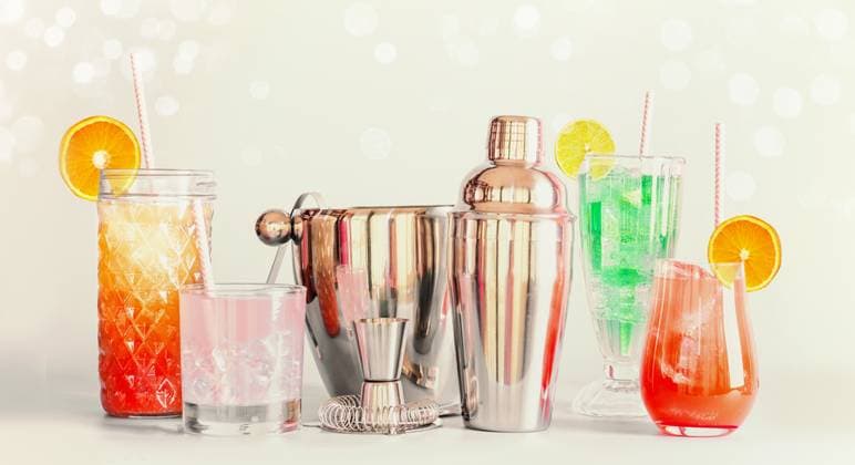Colorful summer long drinks bar and cocktails tools in various glasses with drinking straws and citrus fruits standing at light background ,model released, Symbolfoto