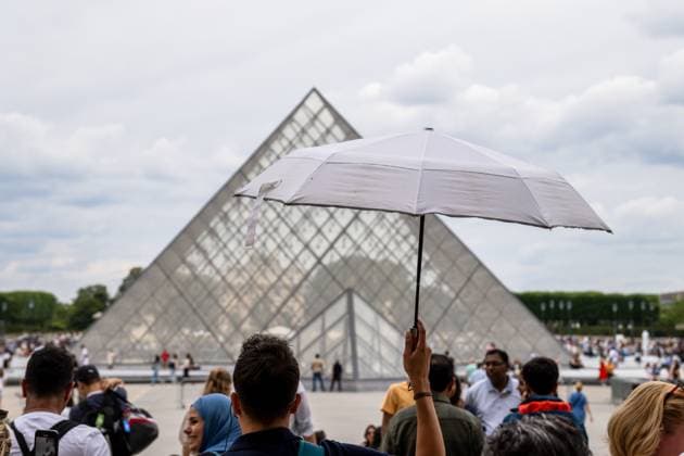 IMAGO Creative, Jahreszeit Sommer, Hitze Paris, France - July 14, 2024: In front of the Louvre Museum in Paris, tourists protect themselves from the summer heat with a parasol while queuing in front of the famous glass pyramid *** Vor dem Louvre-Museum in Paris schützen sich Touristen mit einem Sonnenschirm vor der Hitze im Sommer, während sie in der Warteschlange vor der berühmten Glaspyramide stehen