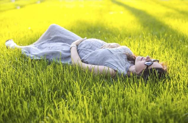 Creative Highlights Symbolbilder Cute pregnant female touching belly gently and sitting on green grass while relaxing in park during sunset in summer Copyright: imageBROKER DashaxPetrenko ibxiqx10540110.jpg ,model released, Symbolfoto ,property released