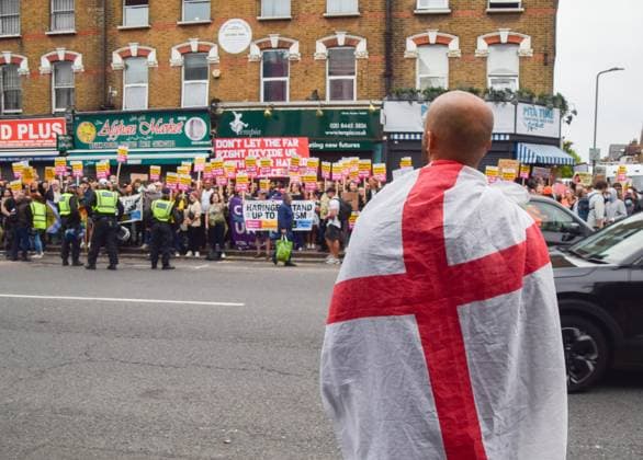 Bilder des Jahres 2024, News 08 August News Themen der Woche KW32 August 7, 2024, London, England, UK: A lone right-wing protester draped in an England flag watches as crowds gather for a rally against the far-right and racism in Finchley following a week of riots organised by the far-right across the UK. The protesters lined the streets near an immigration services office, which was reportedly one of the places on a far-right target list on what was meant to be a day of multiple far-right riots. In the end only a handful of right-wing protesters showed up. London UK - ZUMAv130 20240807_zip_v130_051 Copyright: xVukxValcicx