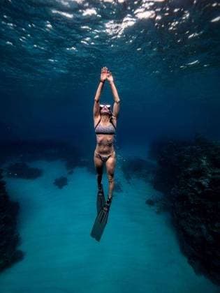 Creative Highlights Symbolbilder A vertical shot of a woman snorkeling underwater in clear blue ocean with coral reefs visible in the background 25470780 ,model released, Symbolfoto RECORD DATE NOT STATED